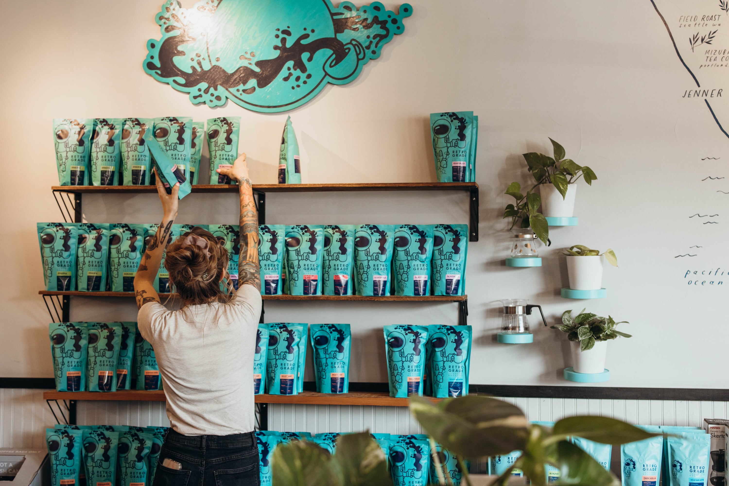 Person arranging teal coffee bags on shelves in a coffee shop.